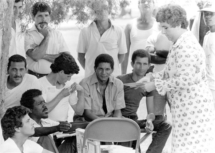 white woman passes out papers to a group of Cuban refugee men