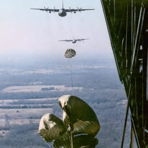 View of two large planes in air with deployed parachutes from inside third airplane