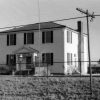 Two-story wood frame building with dark shutters and  "Confederate State Capitol" on the front with rectangular stone monument and barbed wire fence