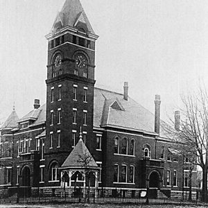 Multistory brick building with clock tower and gazebo inside fence