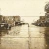 Street wet with rain with brick buildings and storefronts with parked cars