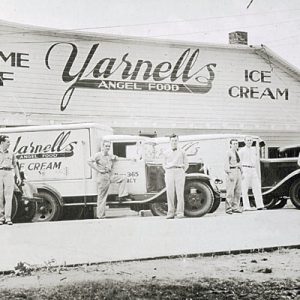 White drivers in uniform pose with their delivery trucks outside Yarnell's Angel-Food building