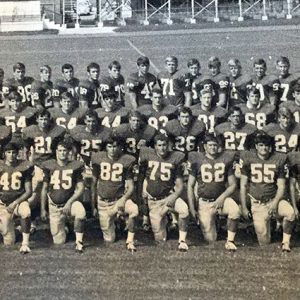 Group of young white and African-American men kneeling and standing in football uniforms on field