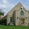 brick church building with A-frame roof and arched windows with cross hanging above them and sign