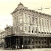 Ornate three-story "First National Bank" building on street corner with covered sidewalk