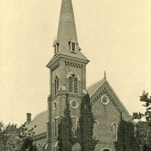 Brick church building with A-frame roof arched windows and door frame with steeple tower on left side