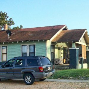 Side view of single-story house with covered porch and satellite dish on the roof with car parked beside it