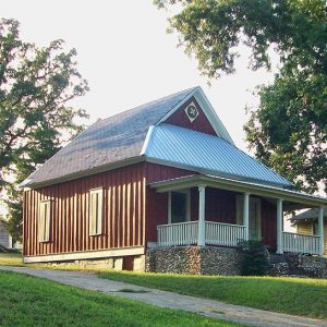 Red house with Dutch gable roof and covered porch on grass