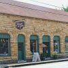 Single-story brick storefront with arched windows doorways and hanging signs on street