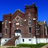 Multistory brick church building with arched multicolored windows and arched doorway on street corner