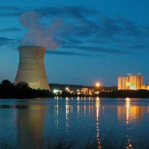 Cooling tower at night emitting steam by waterside power plant