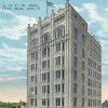 Ten-story building in between much smaller storefronts on city street with parked cars