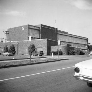 Multistory brick building with balconies on street with power lines and parked cars