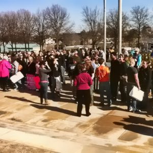 Crowd of women gathered outside with city buildings and trees in the background