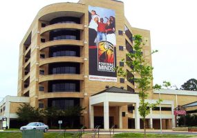 multistory brick and glass building with curved corner sporting large poster featuring diverse students