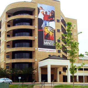 multistory brick and glass building with curved corner sporting large poster featuring diverse students