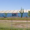 Large blue metal building with "Acme Brick" logo and fence