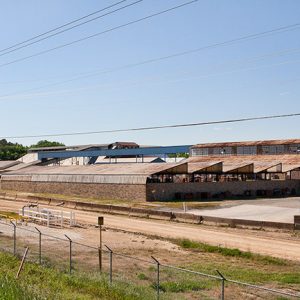 Industrial campus featuring warehouses roofed with sheet metal beyond a fence