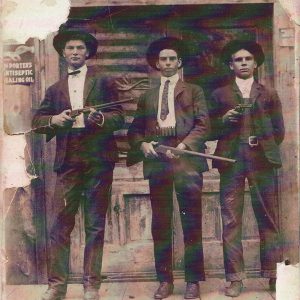 Three men in suits and hats with two holding shotguns and one holding a pistol