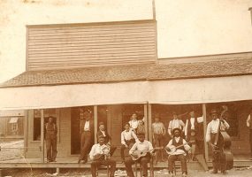 African-American musicians with their instruments and mixed group of patrons outside storefront building