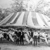 White men and women on carnival ride with striped tent behind them