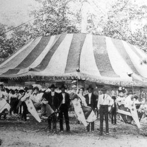 White men and women on carnival ride with striped tent behind them