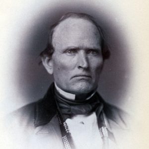 White man with stern expression in suit with white collar