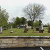 Stone monuments and gravestones with trees in cemetery seen over brick wall