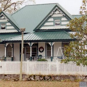 Multistory house with cross-hipped roof and covered porch with white wooden fence