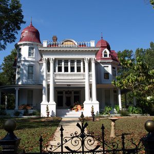 Three-story ornate white house with red round towers and columns with an iron fence