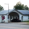 Red and black sports car parked under arched canopy of single-story service station building on street