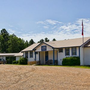 Single-story buildings with covered walkway between them on gravel parking lot