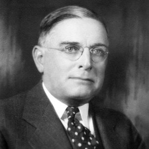 White man with glasses in suit with spotted tie