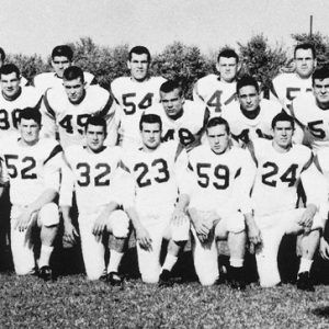 Mixed group of young men in football uniforms and their coaches posing outdoors