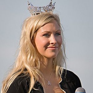 Young white woman with long blonde hair and crown holding a microphone