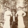 White man in suit and bow tie sitting with wife and daughters standing behind him