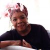 African-American woman in turban and hoop earrings behind orchid