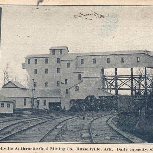 Single and multistory industrial buildings with smoke stack and railroad tracks in the foreground