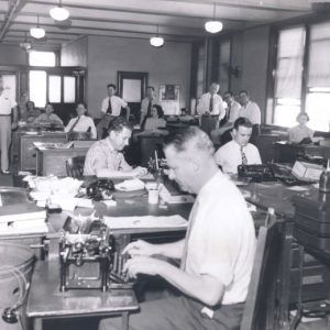 Room full of white men and women working on their typewriters