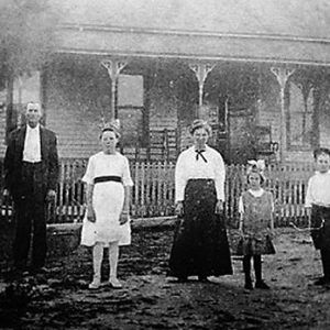 White men women and children standing outside house with covered porch and fence