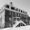 Multistory brick building with cupola on its roof and covered entrance with twin staircases leading to it