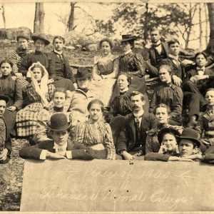 Group of white men in suits and women in skirts and dresses with trees behind them