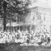 Group of white women and children outside multistory building with balcony and covered porch