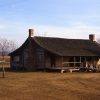 dogtrot-style log cabin with wooden front porch and ramp in vast open field and sign reading "Arkansas County Museum"