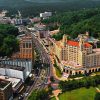 aerial view of downtown Hot Springs featuring the large somewhat triangular shaped Arlington hotel and various other tall buildings and boulevard with cars amid tree-covered hills