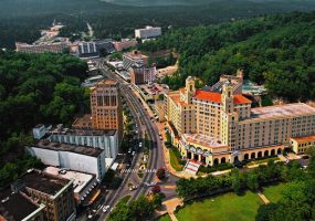 aerial view of downtown Hot Springs featuring the large somewhat triangular shaped Arlington hotel and various other tall buildings and boulevard with cars amid tree-covered hills