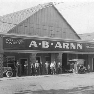 White men standing with cars outside dealership building