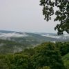 Clouds hovering above tree covered mountains with gray skies