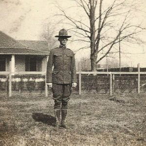 White man standing in military uniform with house fence and tree behind him