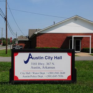 Street with "Austin City Hall" sign and brick building with gas station in the background